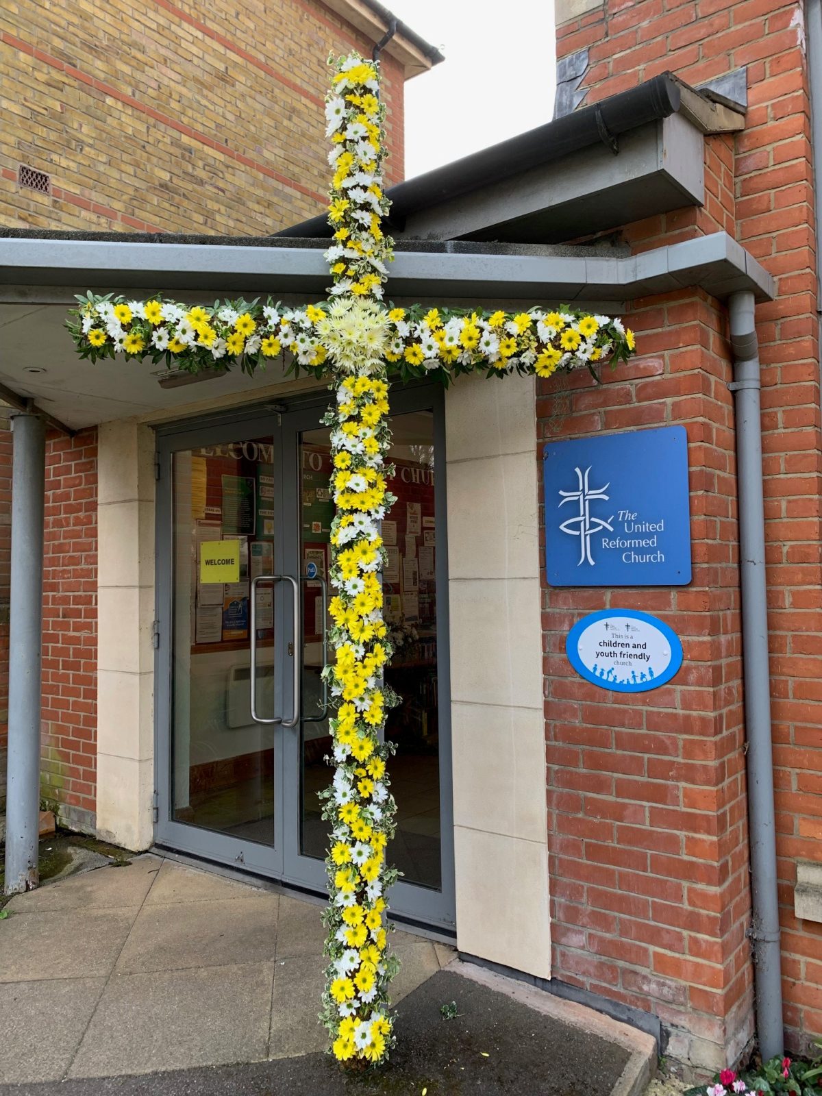 A Cross of yellow and white flowers outside the church entrance.